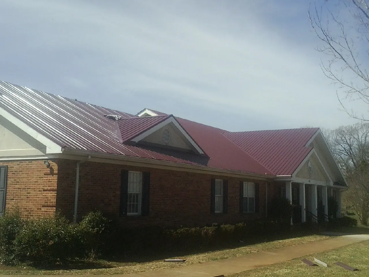 Red metal roof with gabled entries on a long brick building, from a Hail Damage Roof Repair job in Hugo