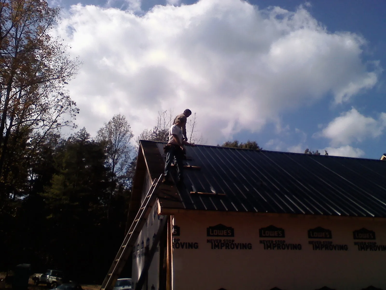 Roofer fastening dark metal panels high against a cloudy sky, from a Roof Inspection job in Hugo