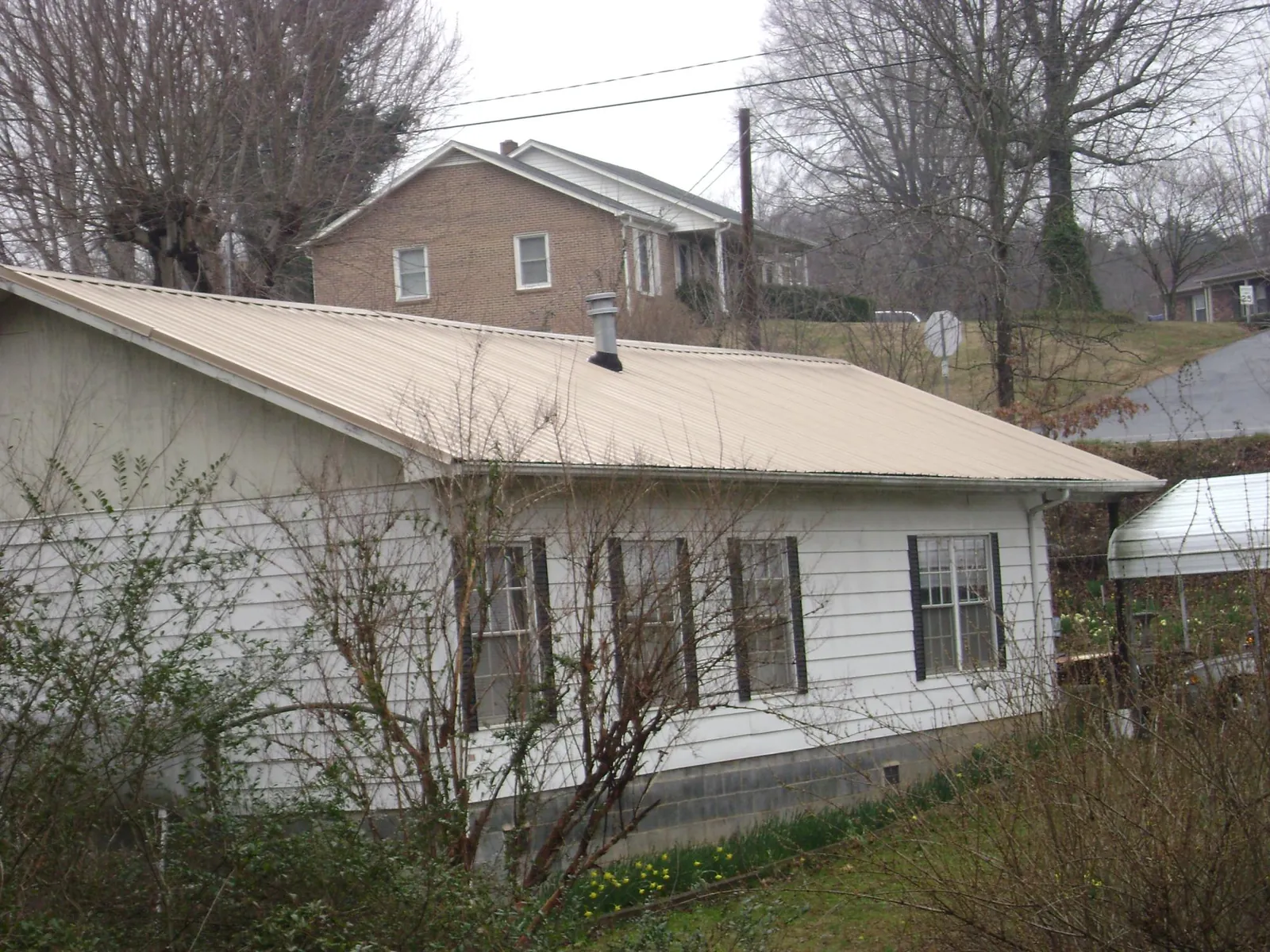 Tan metal roof on a white sided house set into a hillside — Commercial Roofing by Roofing Brothers in Hugo